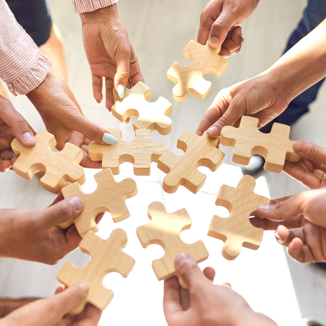 Puzzleteile in mehreren Händen stehen für Teamarbeit in der Fortbildung ehrenamtlicher Leitungsteams.
