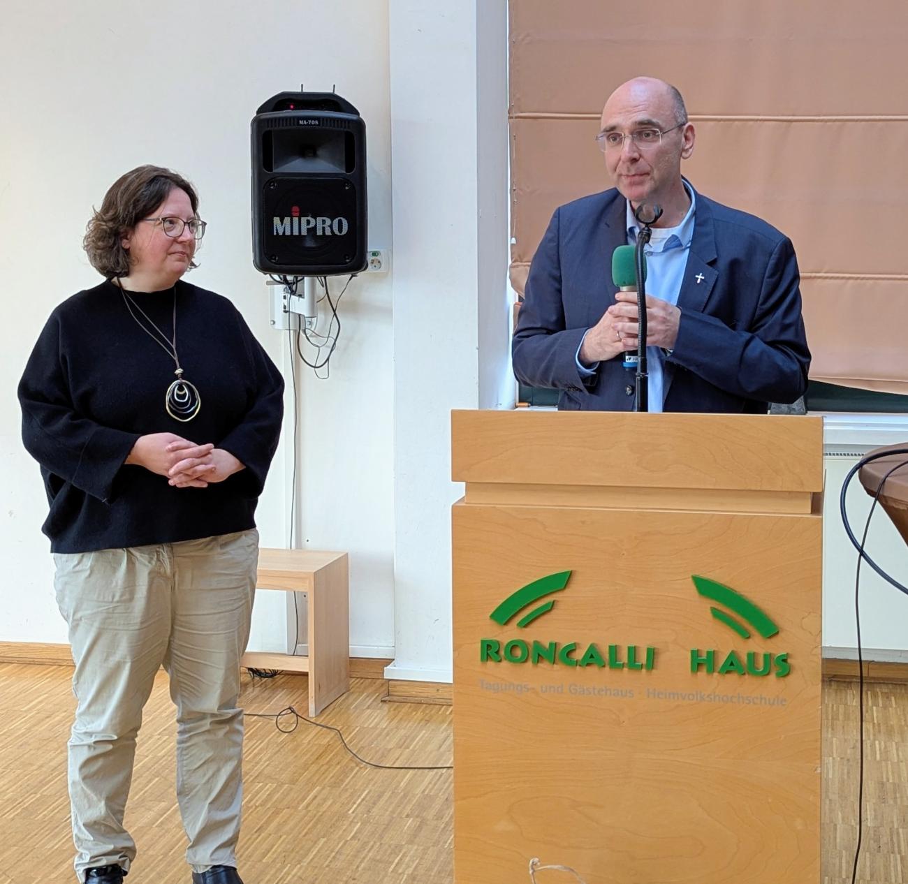 Eine Frau und ein Mann bei einem Vortrag hinter einem Rednerpult.